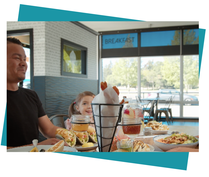 A father and daughter enjoying a delicious meal in Stony Plain, Alberta. The dad has tacos in front of him and there's also a cone filled with sweet potato fries on the table.